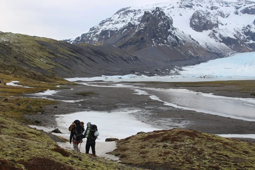 Two guys with big packs on walking towards the mountains
