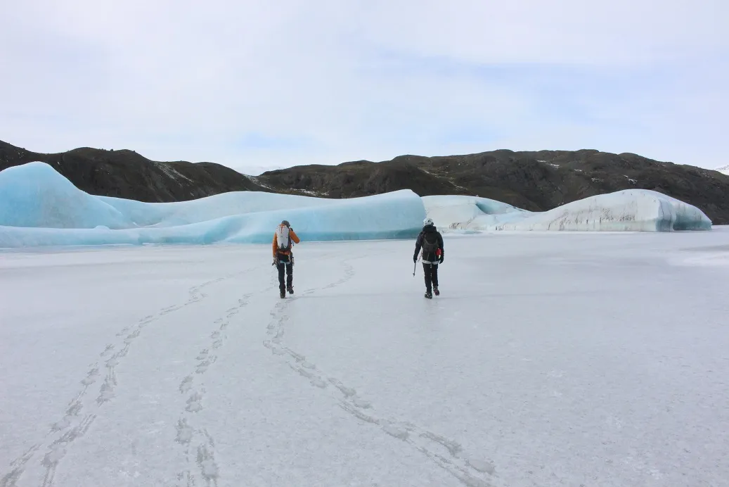 Two guys walking along flat ice between icebergs