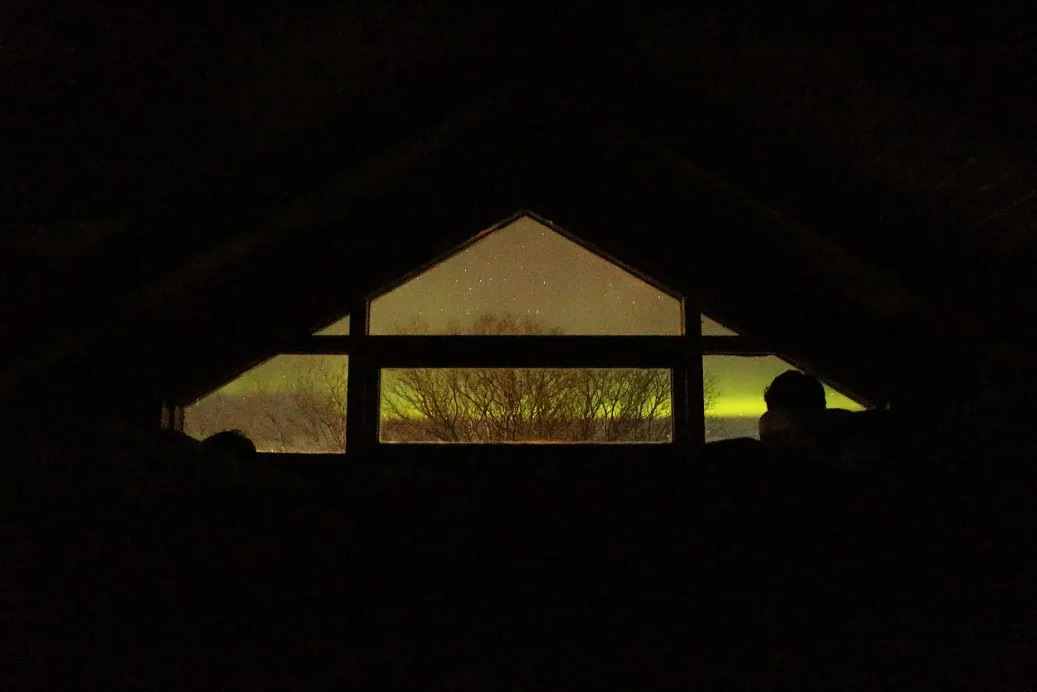 A triangular shaped attic room with the northern lights visible through the window