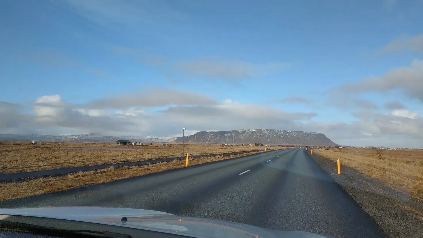View from the front seat of te car, at the desolate and flat landscape, with a mountain in the distance