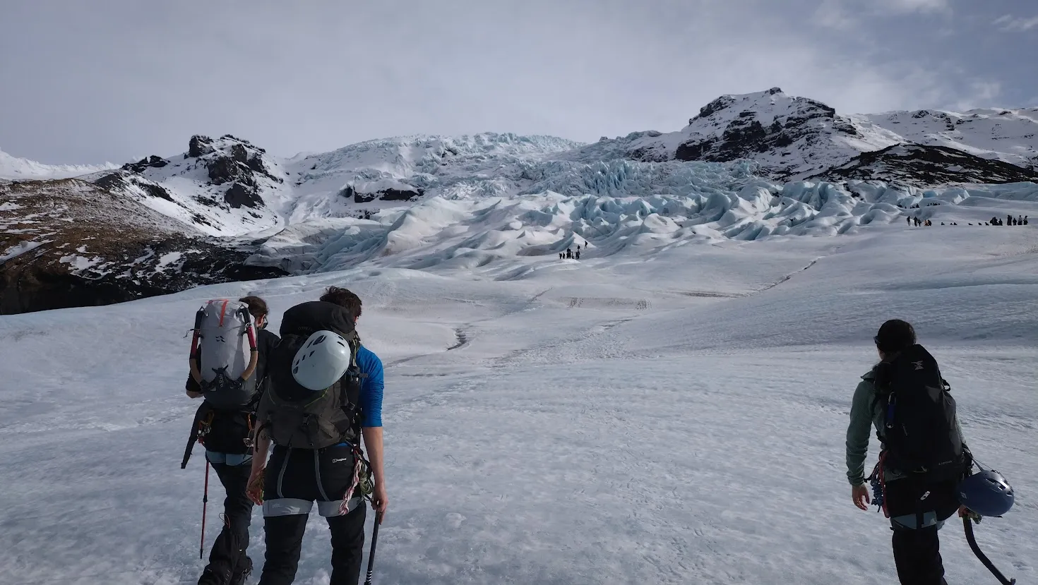 Three people with rucksacks walk on the ice on the lower part of a glacier