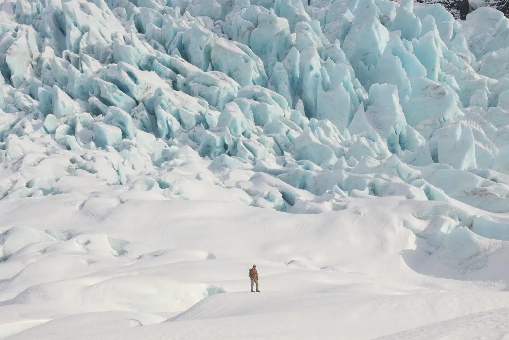 A guy stood on a glacier, dwarfed by the seracs behind him