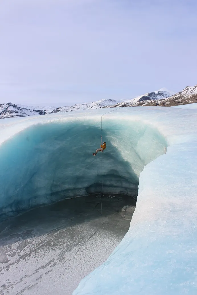 A guy hanging from a rope in front of a huge ice cave