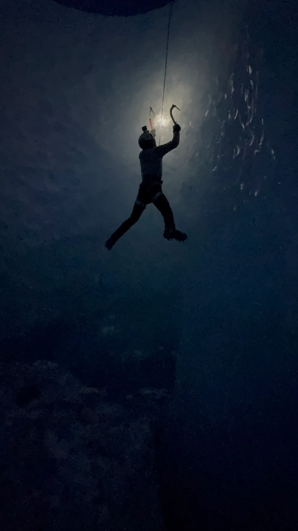 A man climbs a vertical ice wall in the darkness with his head torch on