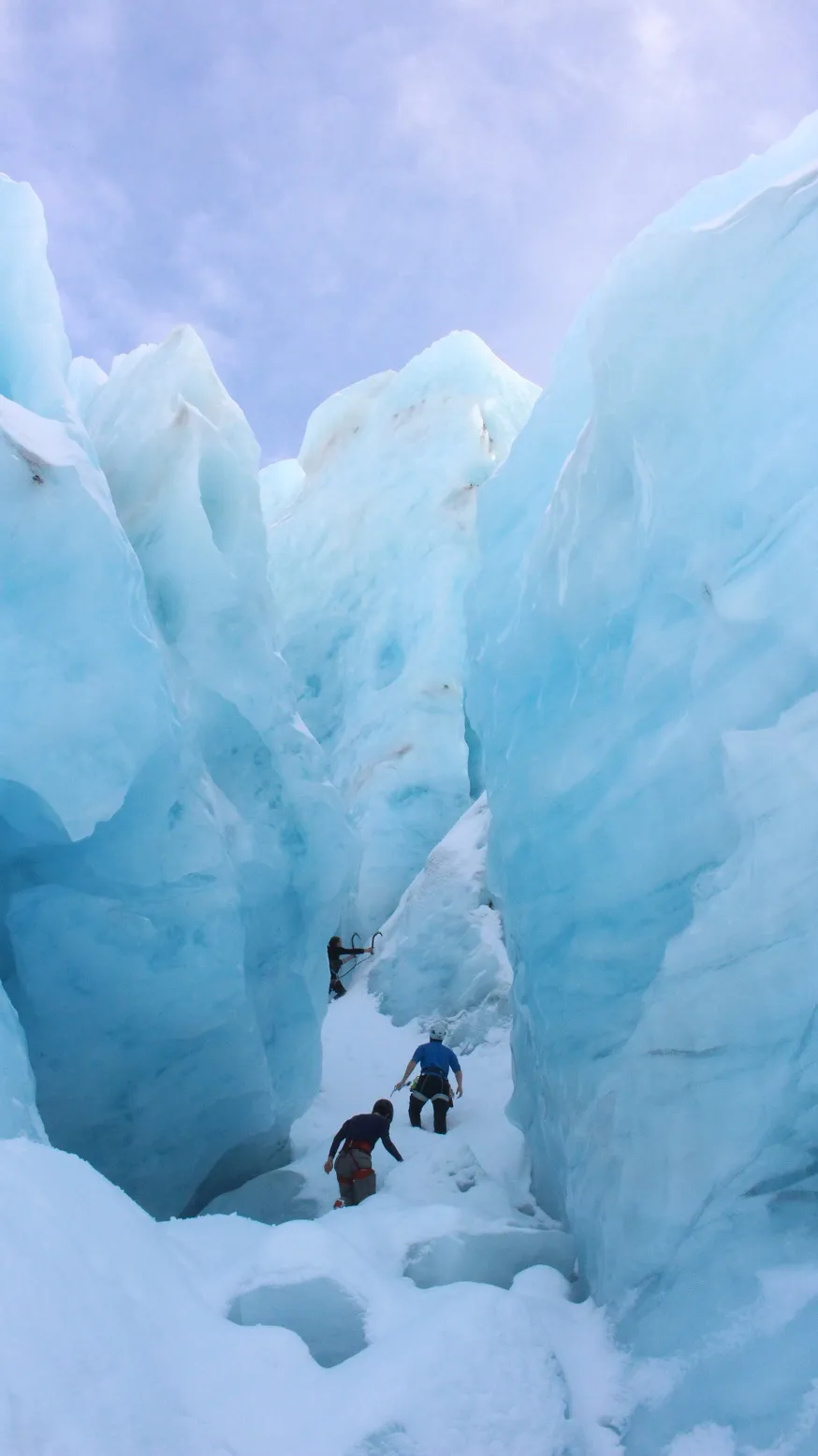 Three people exploring the glacier. The seracs tower like buildings over them